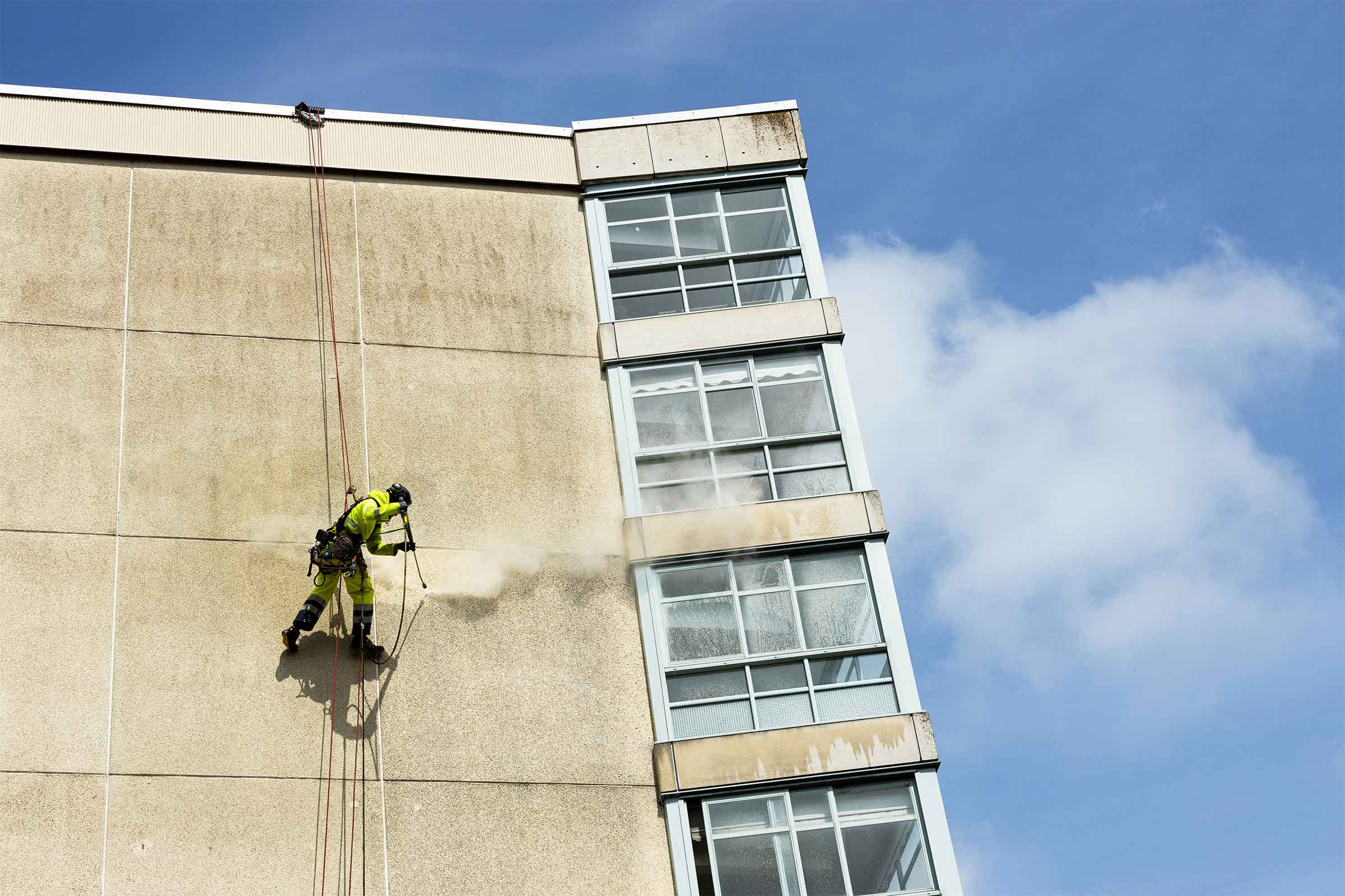 Man hängandes och högtryckstvättar fasad