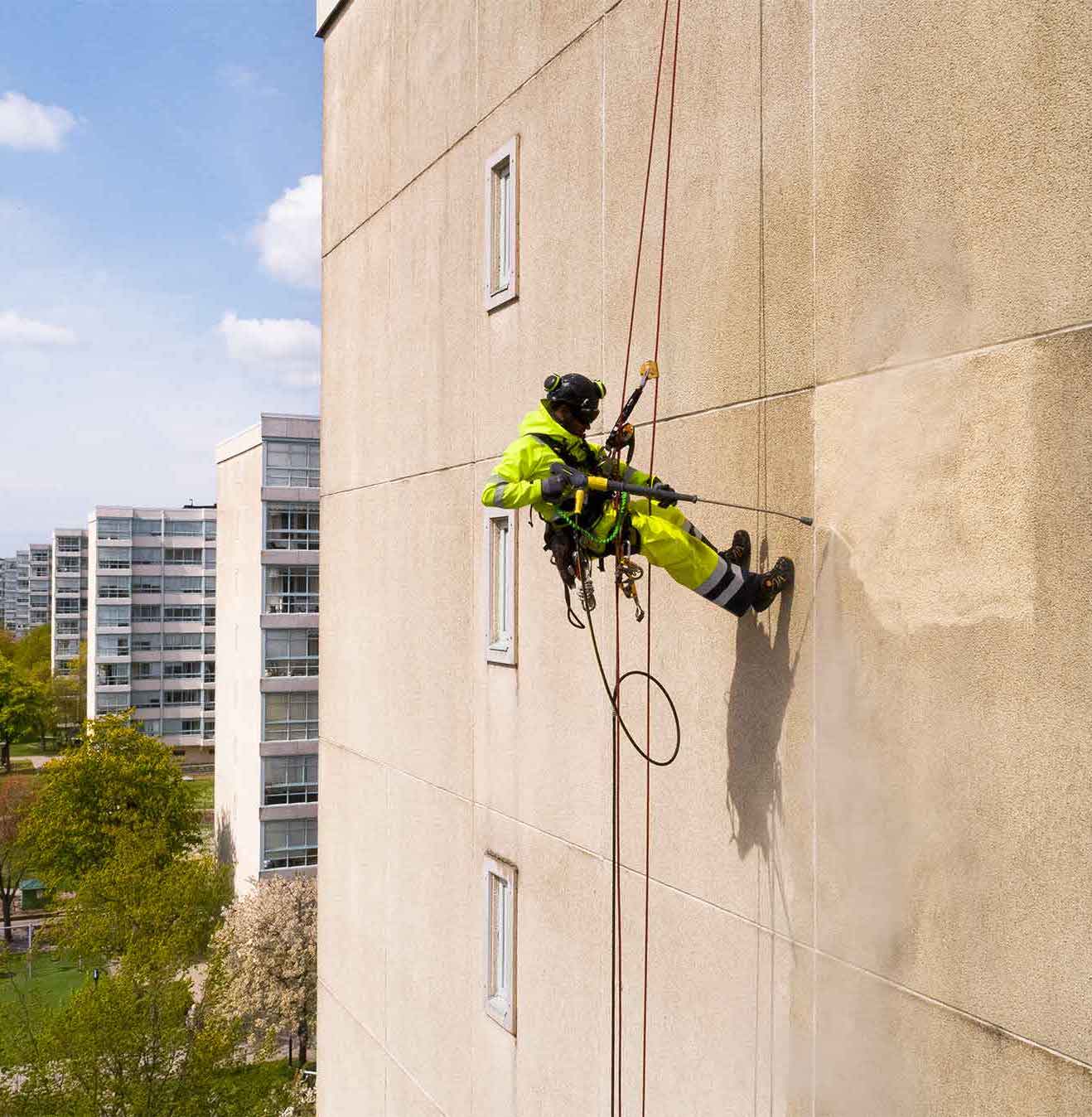 högtryckstvättning på fasad av person hängandes i sele